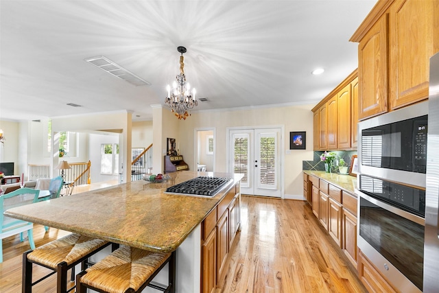 kitchen with a center island, stainless steel appliances, light wood finished floors, and a notable chandelier