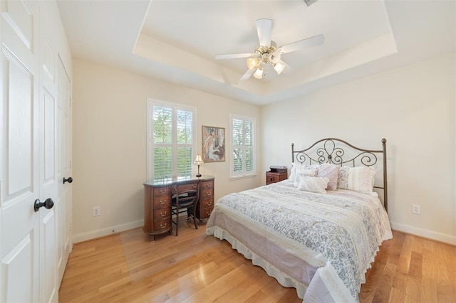 bedroom featuring light wood-style floors, a raised ceiling, ceiling fan, and baseboards