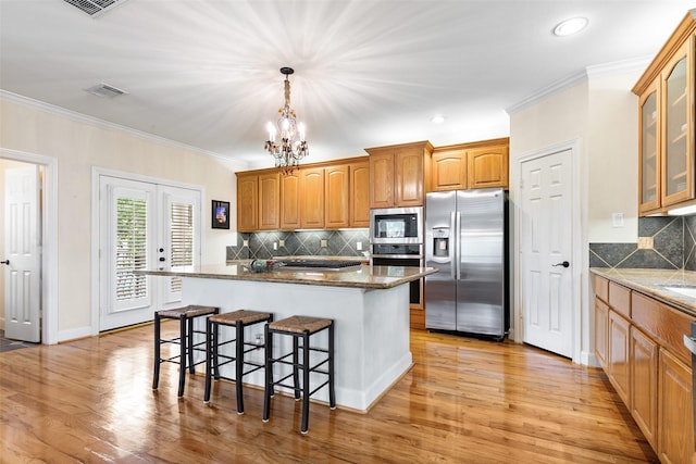 kitchen with visible vents, glass insert cabinets, a kitchen breakfast bar, backsplash, and stainless steel appliances