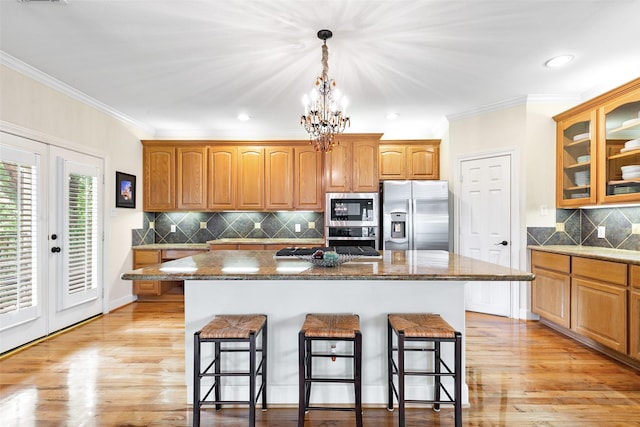 kitchen featuring crown molding, glass insert cabinets, a kitchen bar, a center island, and stainless steel appliances