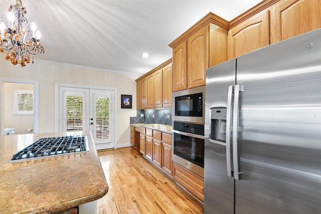 kitchen with ornamental molding, light stone counters, light wood finished floors, appliances with stainless steel finishes, and a notable chandelier