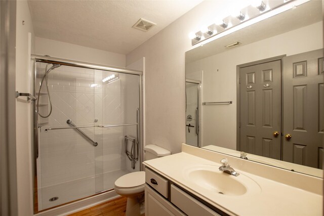 full bathroom with vanity, toilet, wood finished floors, visible vents, and a stall shower