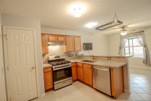 kitchen featuring appliances with stainless steel finishes, tasteful backsplash, a sink, under cabinet range hood, and light tile patterned flooring