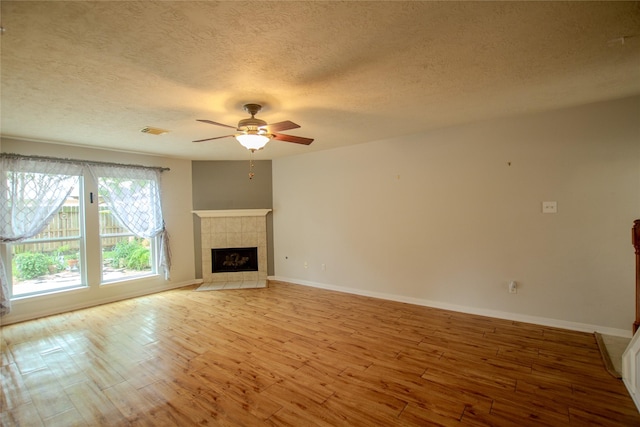 unfurnished living room featuring visible vents, light wood-style floors, a textured ceiling, a tile fireplace, and a ceiling fan