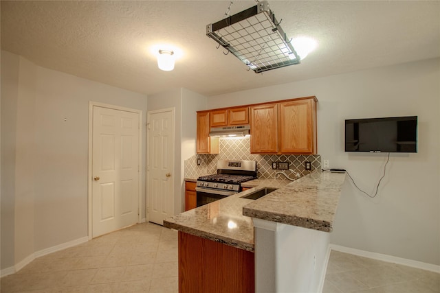 kitchen featuring baseboards, stainless steel gas range oven, under cabinet range hood, light stone counters, and backsplash
