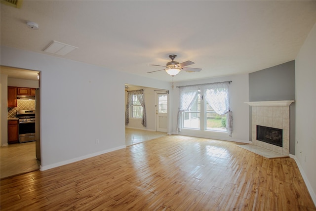 unfurnished living room with a ceiling fan, visible vents, a tiled fireplace, light wood-type flooring, and baseboards