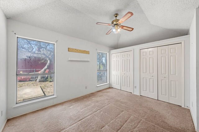 unfurnished bedroom featuring a textured ceiling, multiple closets, ceiling fan, and carpet