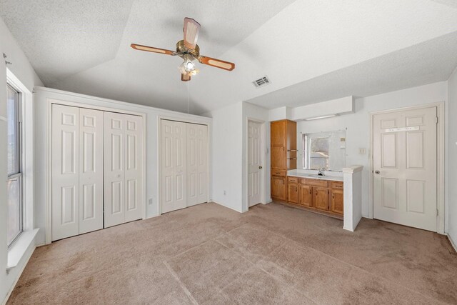 unfurnished bedroom with light carpet, a sink, multiple closets, lofted ceiling, and visible vents