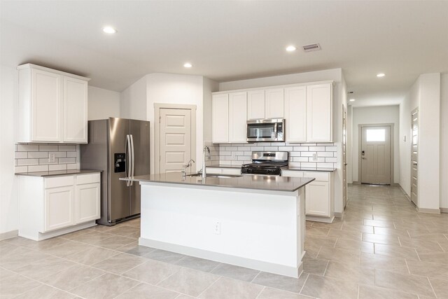 kitchen with appliances with stainless steel finishes, a sink, an island with sink, white cabinetry, and tasteful backsplash
