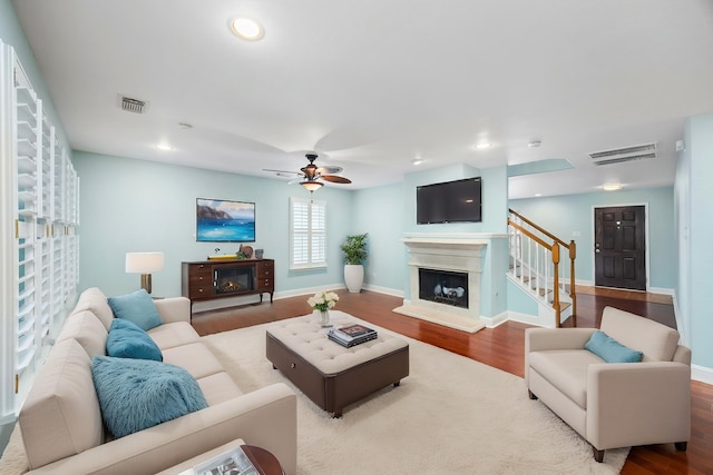 living area with visible vents, a fireplace with raised hearth, and wood finished floors