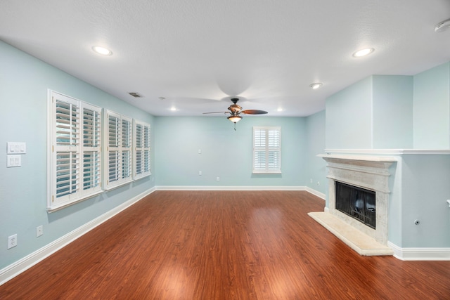 unfurnished living room with baseboards, a fireplace with raised hearth, ceiling fan, and wood finished floors