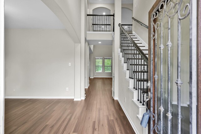foyer entrance featuring stairs, arched walkways, baseboards, and wood finished floors