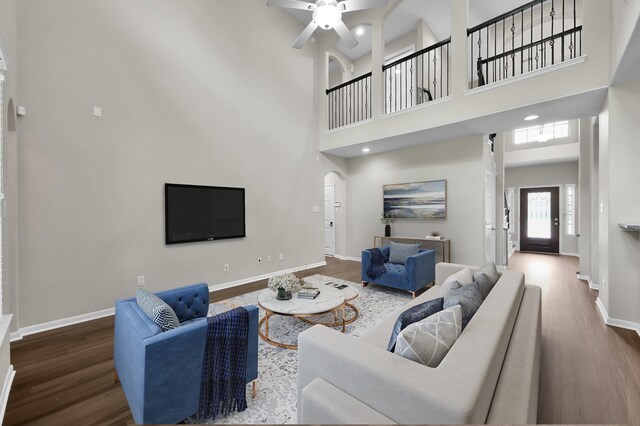 living room featuring ceiling fan, arched walkways, wood finished floors, baseboards, and a high ceiling