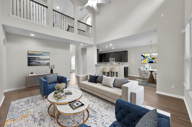 living room with wood finished floors, baseboards, ceiling fan with notable chandelier, and a high ceiling