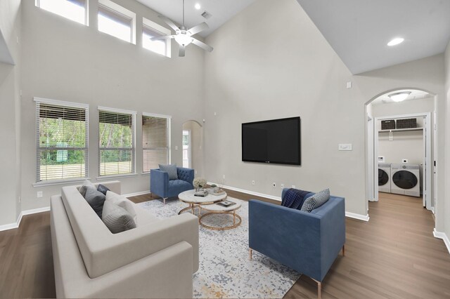 living room featuring arched walkways, plenty of natural light, wood finished floors, and a towering ceiling