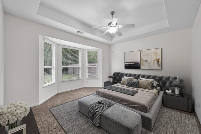 carpeted bedroom featuring a raised ceiling, baseboards, a ceiling fan, and visible vents