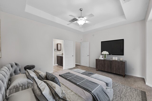 bedroom featuring a tray ceiling, light carpet, baseboards, and ensuite bath