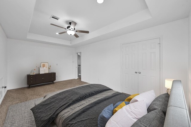 bedroom featuring carpet flooring, ceiling fan, a tray ceiling, visible vents, and a closet