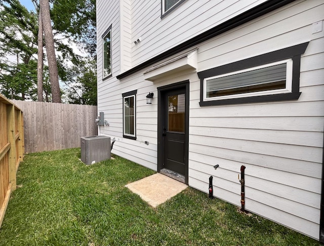 view of exterior entry featuring central AC unit, fence, and a yard