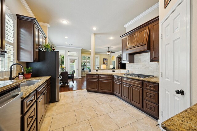kitchen with crown molding, light stone countertops, appliances with stainless steel finishes, a sink, and a peninsula