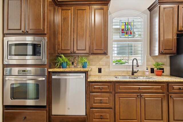 kitchen with backsplash, light stone countertops, appliances with stainless steel finishes, and a sink