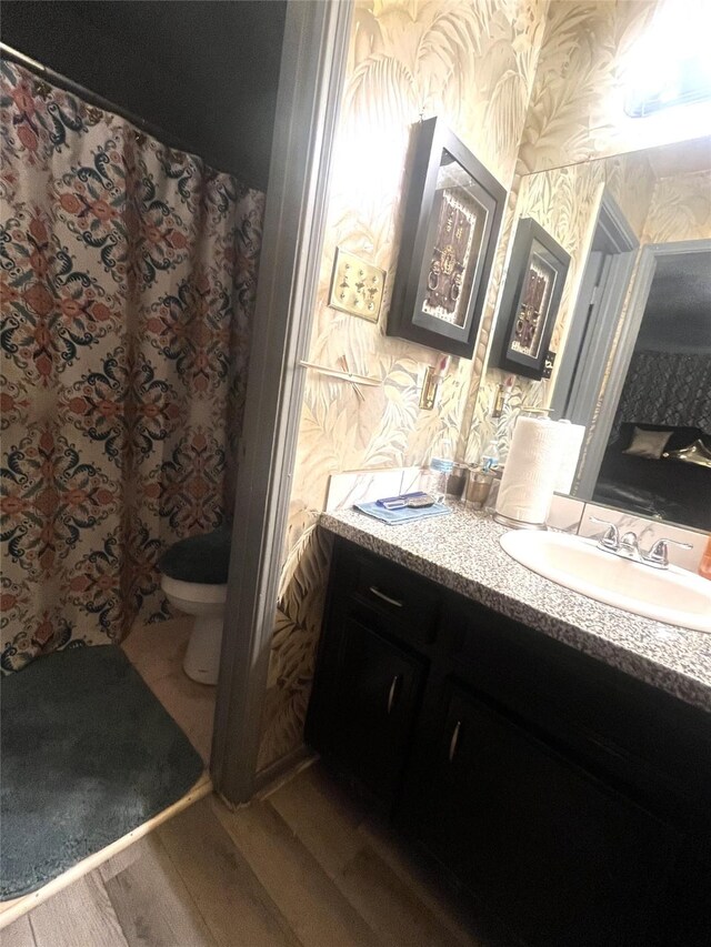 full bath with toilet, wallpapered walls, wood finished floors, and vanity