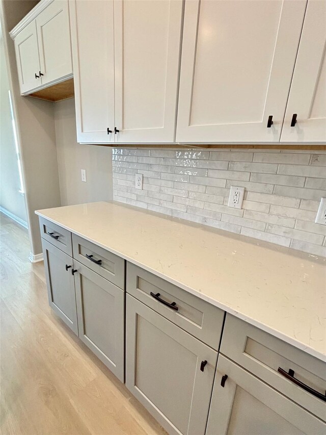 kitchen with light stone countertops, baseboards, light wood finished floors, backsplash, and gray cabinetry