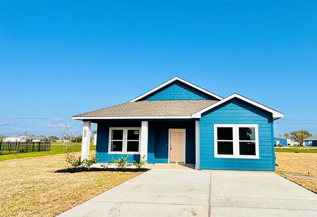 bungalow-style house featuring a porch, a front lawn, roof with shingles, and fence