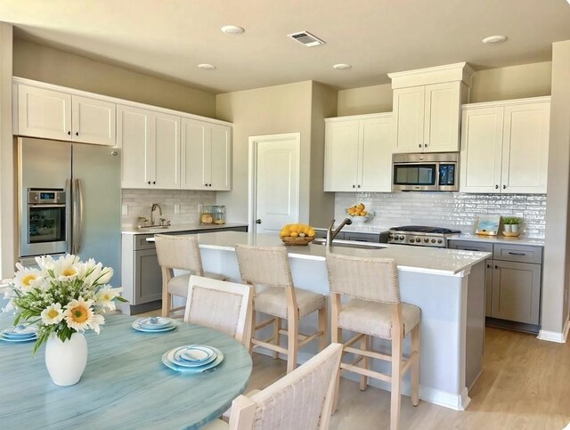 kitchen featuring decorative backsplash, visible vents, appliances with stainless steel finishes, a sink, and an island with sink