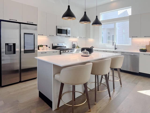kitchen with decorative backsplash, a kitchen island, a breakfast bar area, light wood-type flooring, and stainless steel appliances