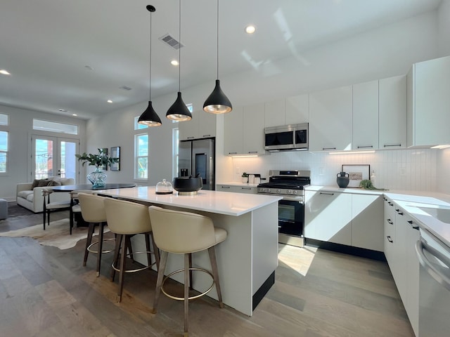 kitchen with visible vents, appliances with stainless steel finishes, a center island, white cabinets, and light wood-style floors