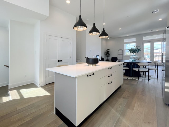 kitchen with a kitchen island, visible vents, hanging light fixtures, white cabinets, and light wood-style flooring