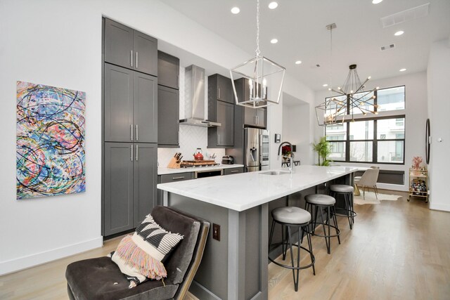 kitchen featuring wall chimney range hood, stainless steel appliances, a chandelier, a sink, and light countertops