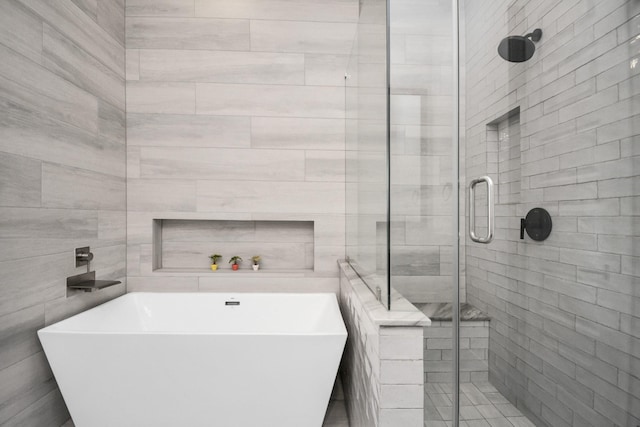 full bath featuring a shower stall, a freestanding tub, and tile walls