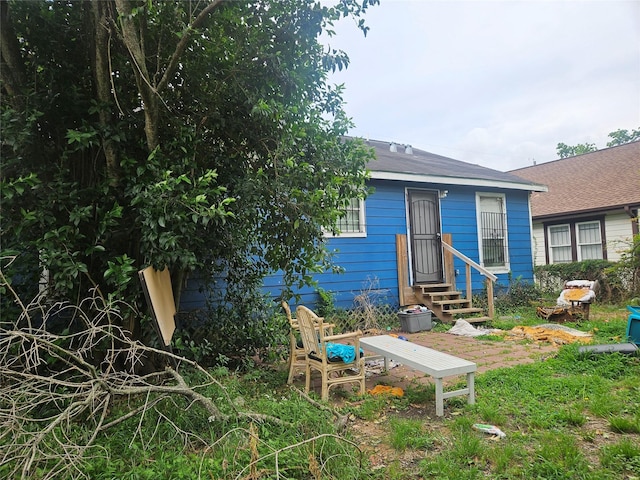 rear view of house featuring entry steps and a shingled roof