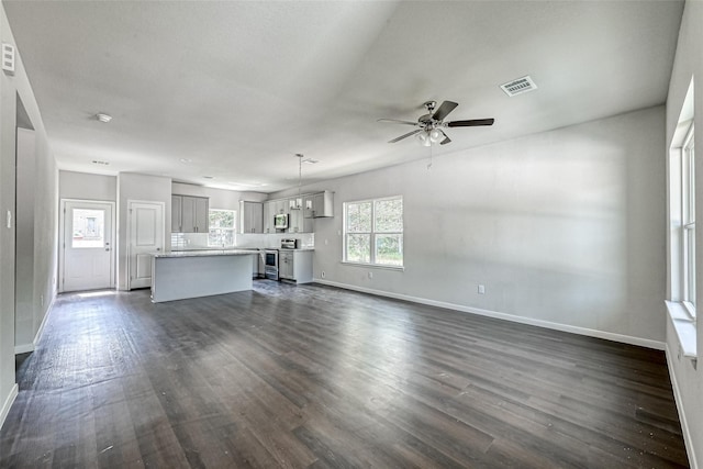 unfurnished living room featuring baseboards, dark wood finished floors, ceiling fan, and visible vents