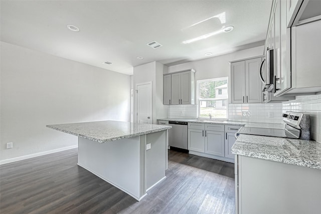 kitchen with decorative backsplash, a kitchen island, dark wood-type flooring, appliances with stainless steel finishes, and gray cabinetry