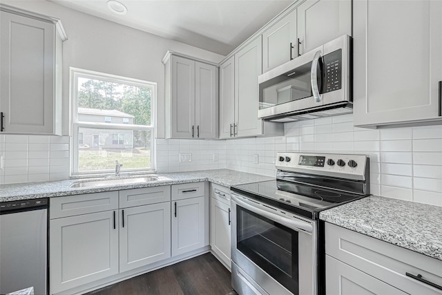 kitchen with a sink, appliances with stainless steel finishes, dark wood-style floors, and light stone countertops