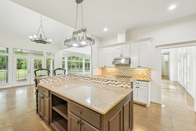 12061 Oak Forest Ln, Conroe, TX 77385 - kitchen featuring under cabinet range hood, white cabinets, light tile patterned flooring, a kitchen island, and decorative backsplash