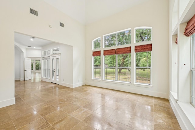 unfurnished living room featuring a towering ceiling, baseboards, arched walkways, and visible vents