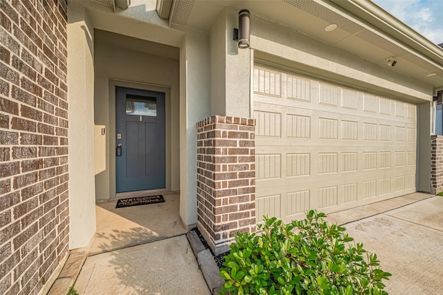 doorway to property with brick siding, a garage, and stucco siding