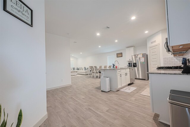 kitchen with decorative backsplash, a sink, open floor plan, stainless steel appliances, and light wood-style flooring