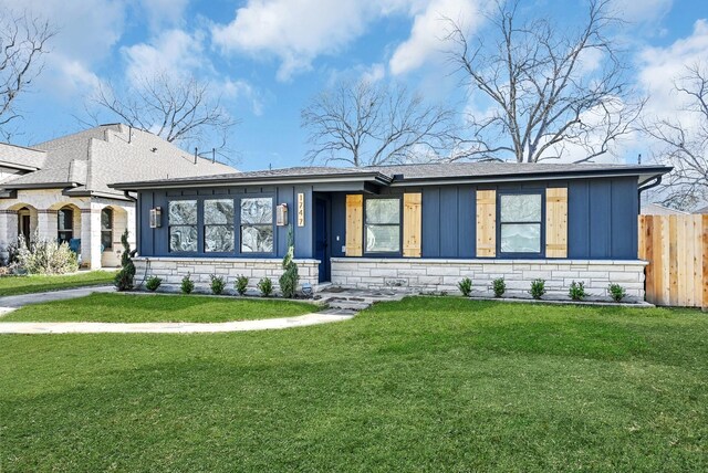view of front of house featuring board and batten siding, fence, stone siding, a shingled roof, and a front yard
