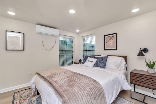 bedroom featuring recessed lighting, wood finished floors, baseboards, and an AC wall unit