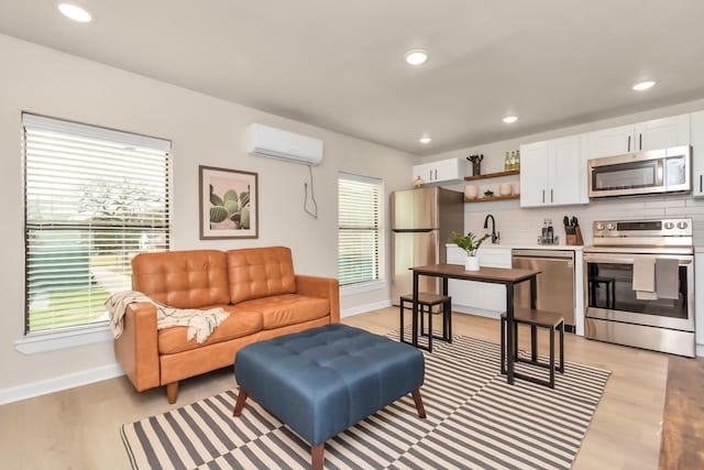 living area featuring baseboards, a healthy amount of sunlight, light wood-style flooring, and a wall unit AC