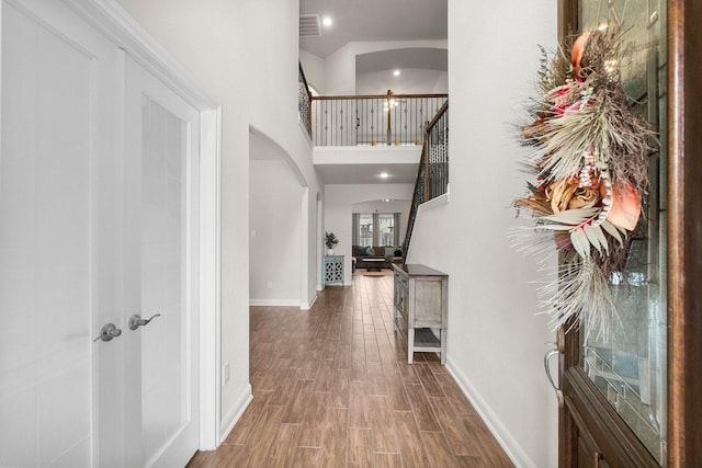 corridor featuring arched walkways, stairs, baseboards, wood finished floors, and a towering ceiling