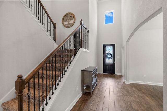 entryway with arched walkways, plenty of natural light, dark wood-style flooring, and a towering ceiling