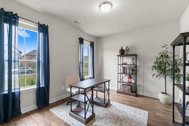 office space featuring a healthy amount of sunlight, baseboards, wood finished floors, and visible vents