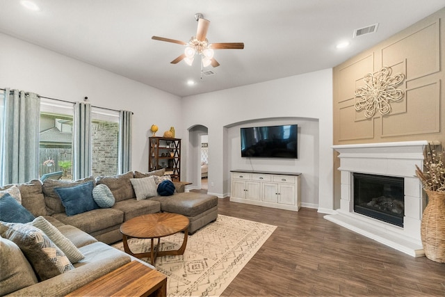 living room featuring arched walkways, a ceiling fan, visible vents, and dark wood-type flooring