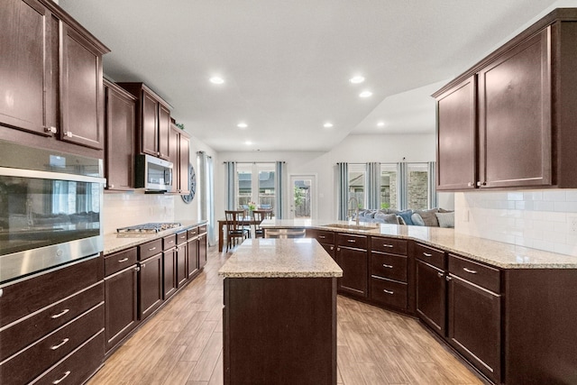 kitchen with appliances with stainless steel finishes, a sink, light wood finished floors, a peninsula, and decorative backsplash